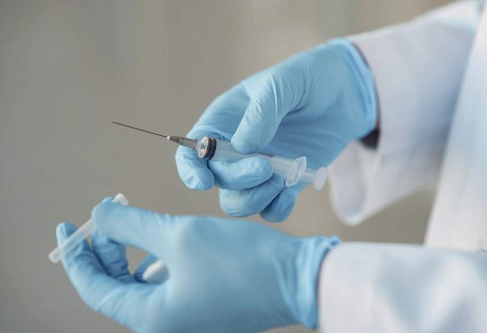 Close-up of doctor’s gloved hands preparing syringe for anaesthesia before Vaser liposuction procedure