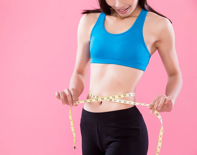 Woman measuring slim waist with tape after liposuction and body contouring
