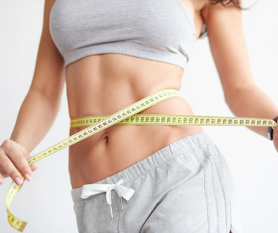 Close-up of fit woman in grey sportswear measuring slim waist with tape after liposuction treatment
