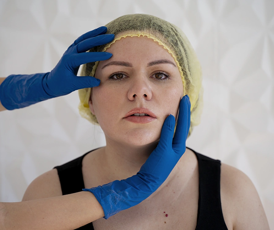 Close-up of surgeon’s gloved hands examining female patient’s face before cosmetic procedure